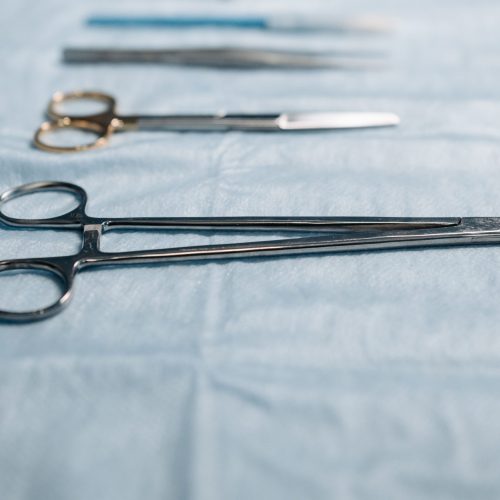 Close-up of surgical tools including a needle holder on a blue cloth in a medical setting.